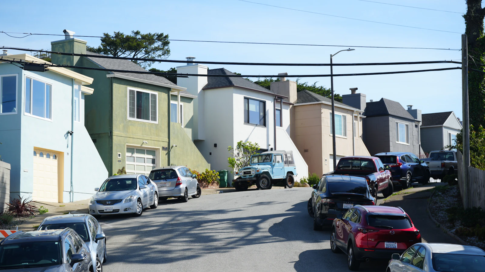 A sloped San Francisco residential street with varied homes and parked cars.