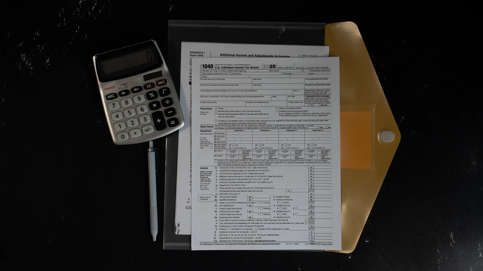 Federal tax forms, a calculator and planning notes arranged on a dark desk.