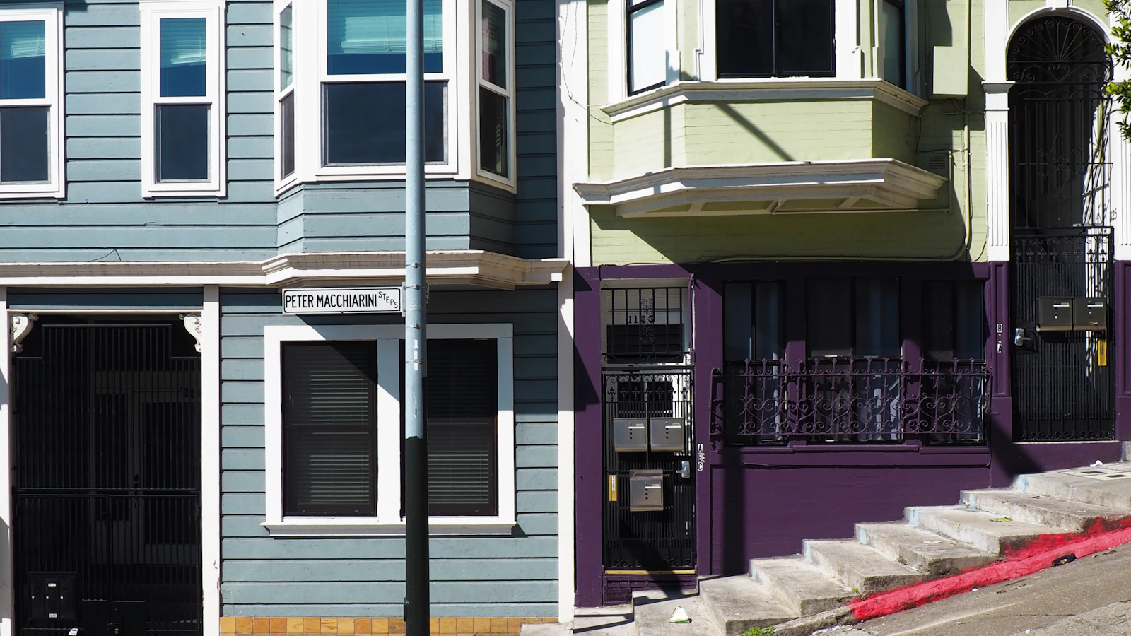 Bay windows and front entrances of homes beside a San Francisco sidewalk.